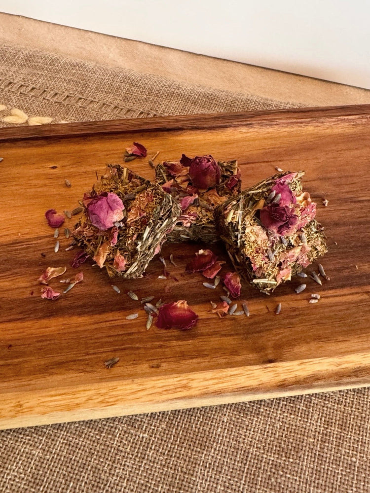 Handmade botanical forage bars for rabbits with dried herbs, flowers, and hay-based ingredients on linen cloth nad wooden board