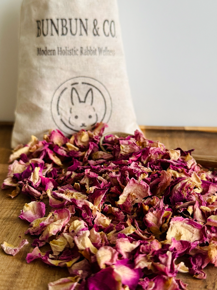 Dried pink rose petals on a wooden surface with a &