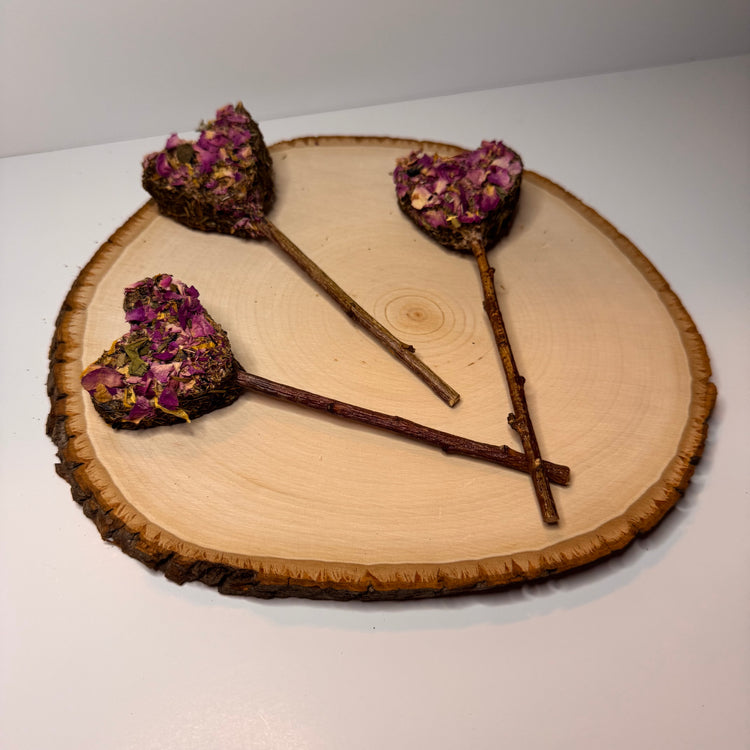 Heart-shaped rabbit forage pops with dried rose petals, botanicals and a peach wood chew stick handles displayed on natural wood slice