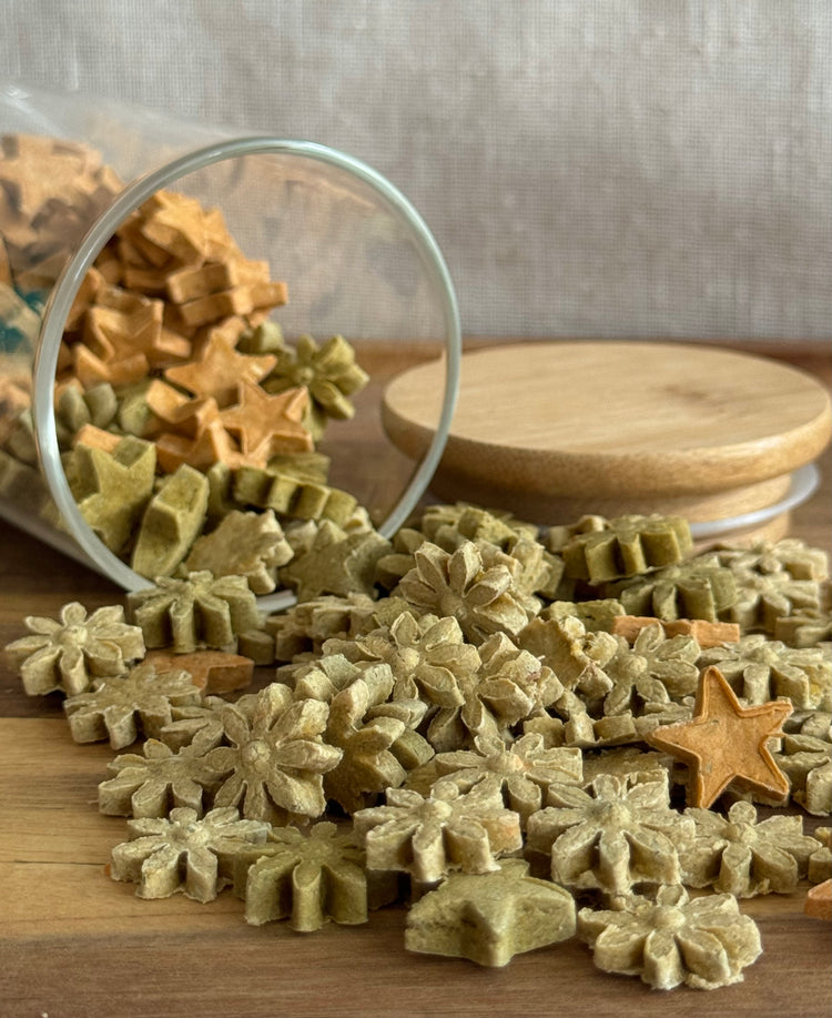 Star- & blossom shaped rabbit treats spilling out of a glass jar onto a wooden surface.