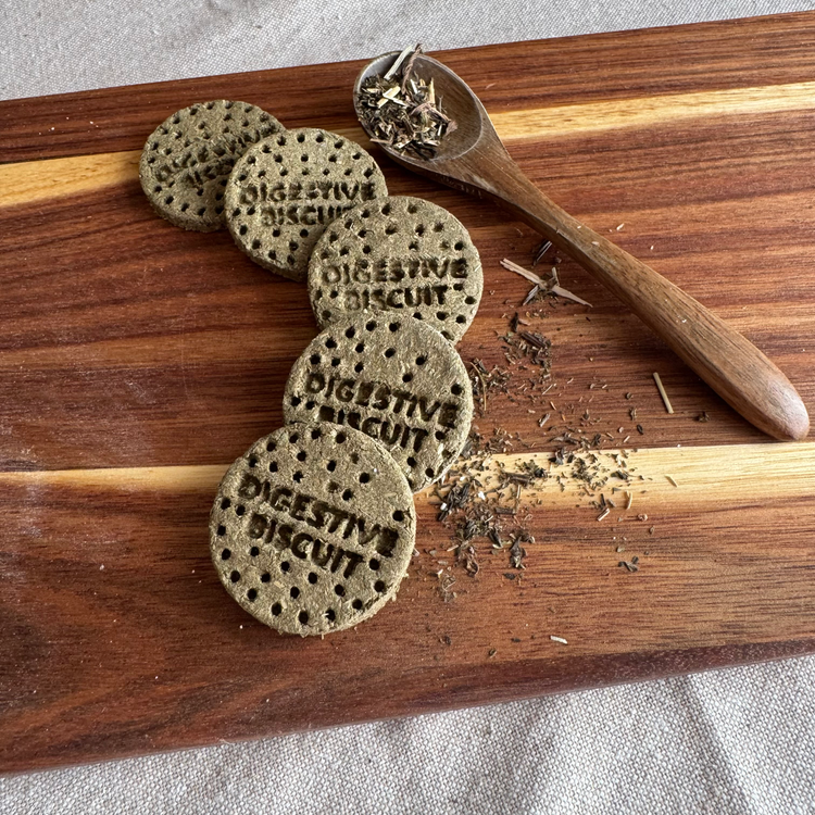 Botanical digestive rabbit biscuits stamped "digestive biscuit" on wooden board with dried herbs and wooden spoon