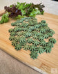 Small green blossom- shaped rabbit treats displayed on a light brown cutting board with fresh greens in the background.