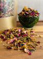 Dried  rabbit forage of flowers and herbs on a wooden surface with a green glass bowl and packaging in the background.