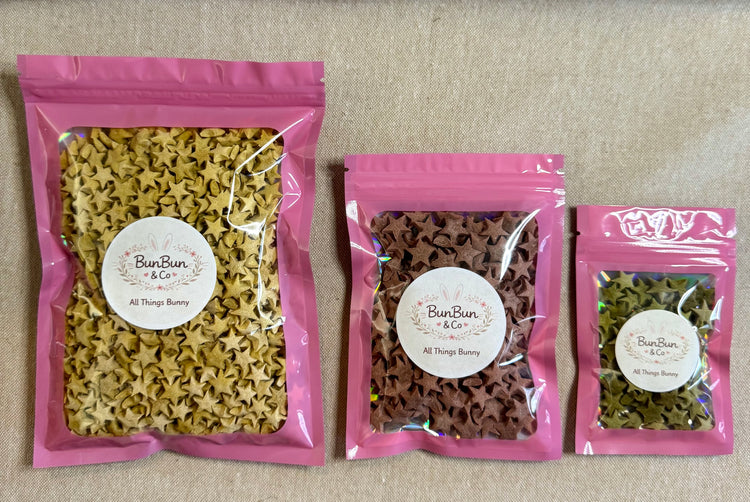 Three pink and clear resealable mylar bags holding yellow,  pink/berry and green colored star shaped rabbit treats with a light colored backround.