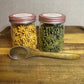  Yellow and green star-shaped rabbit  treats inside two clear apothecary jars with a wooden spoon sitting on a wooden tray