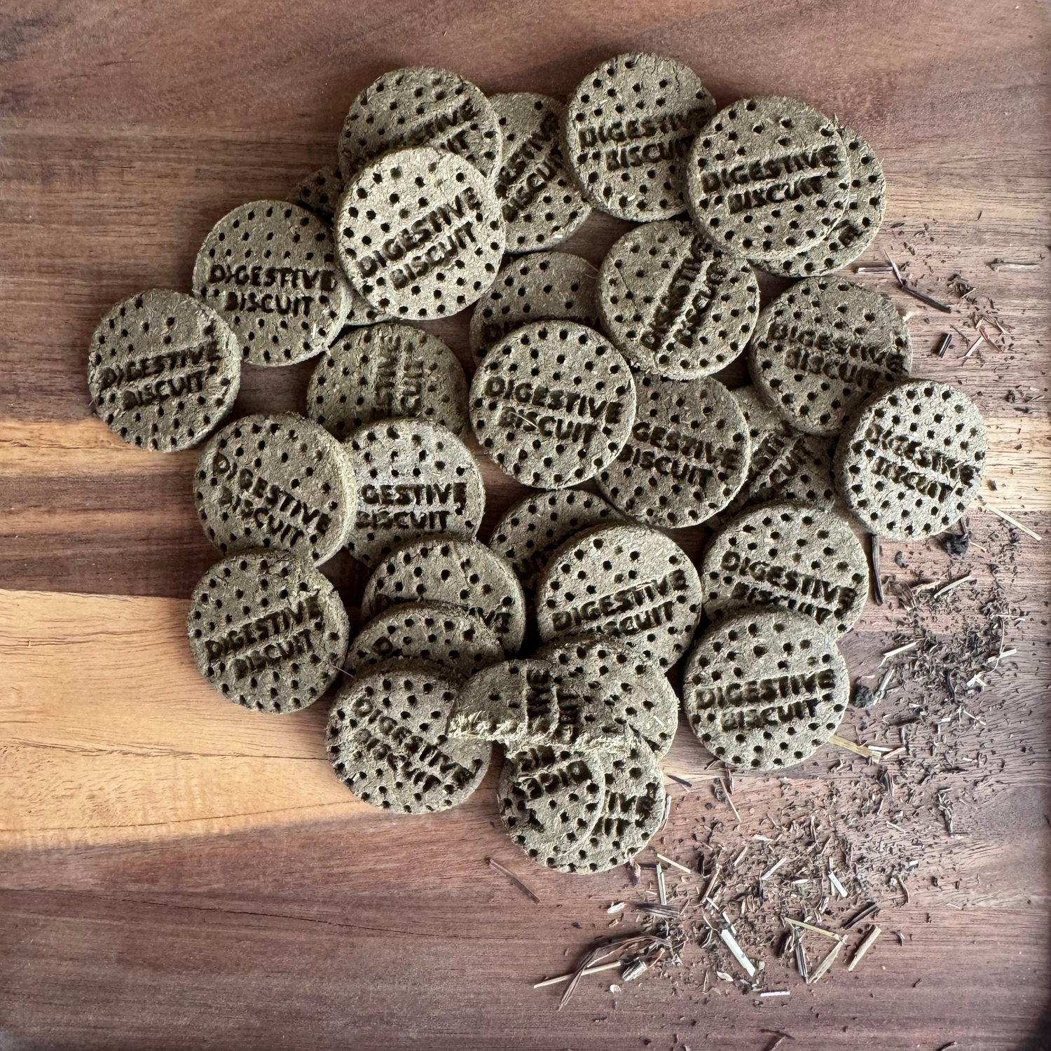 Small batch botanical digestive biscuits for rabbits arranged on a wooden board with scattered herbal blend