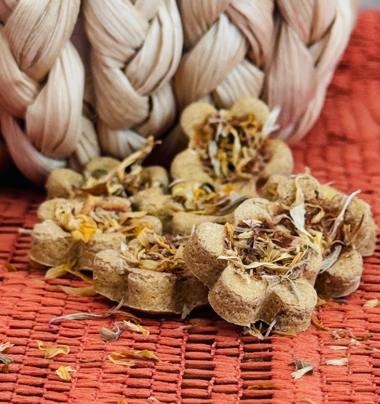 Flower-shaped herbal rabbit treats, displayed on a orange woven mat with a braided beige rope pumpkin in the background.