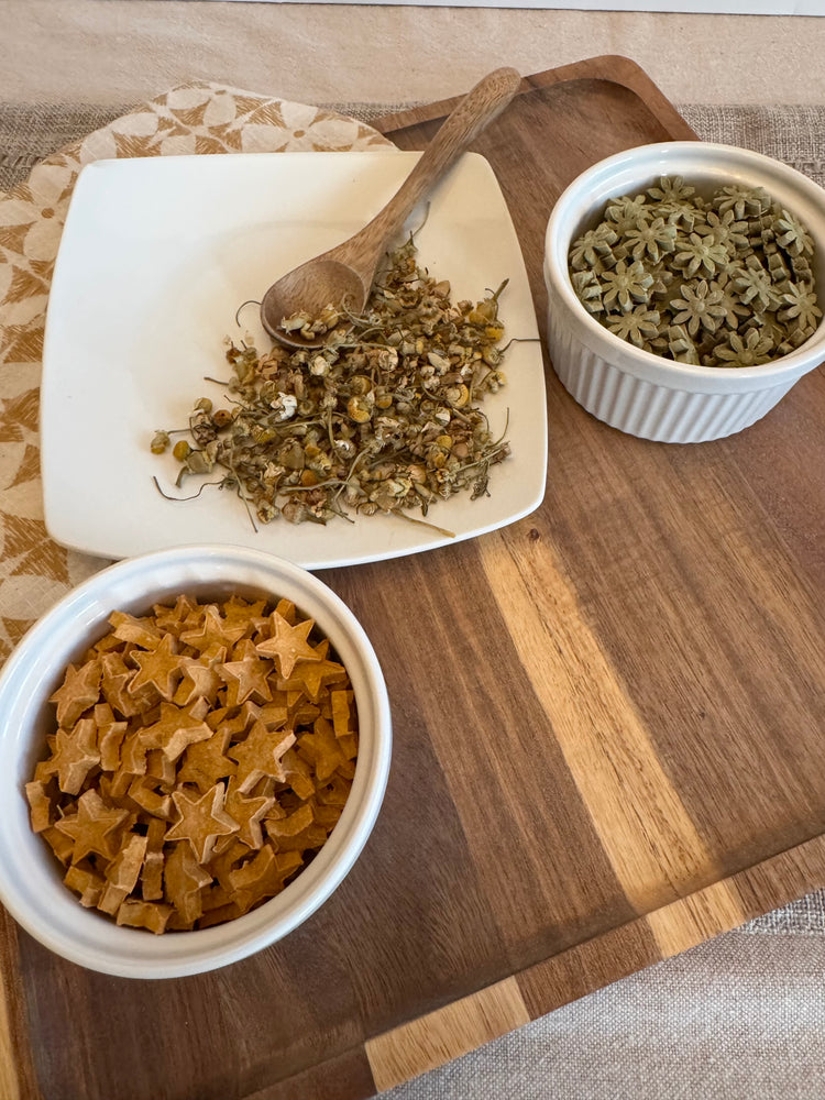 Two bowls of star-shaped rabbit treats on a wooden cutting board with a white plate and wooden spoon.