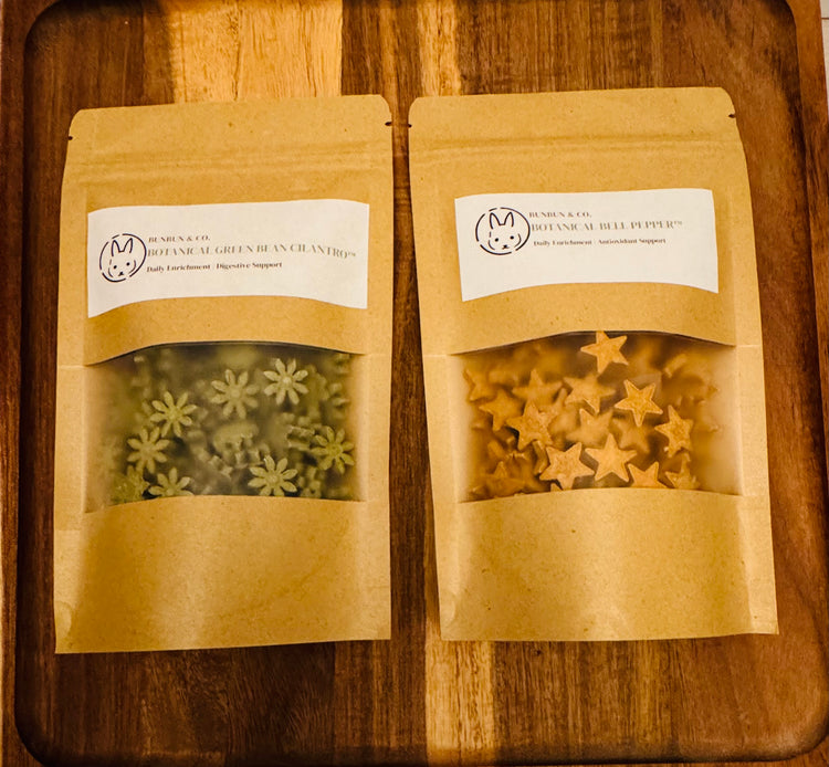 Two  BunBun & Co. brown kraft pouches  with star & blossom shaped rabbit treats on a wooden board.