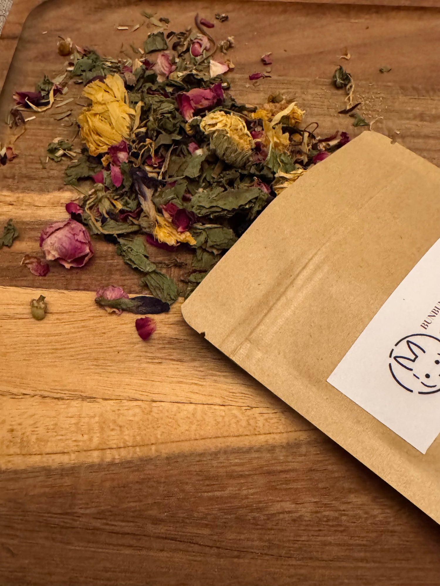  Floral Meadow Forage Blend with dried herbs and flowers on a wooden surface with a brown kraft package.