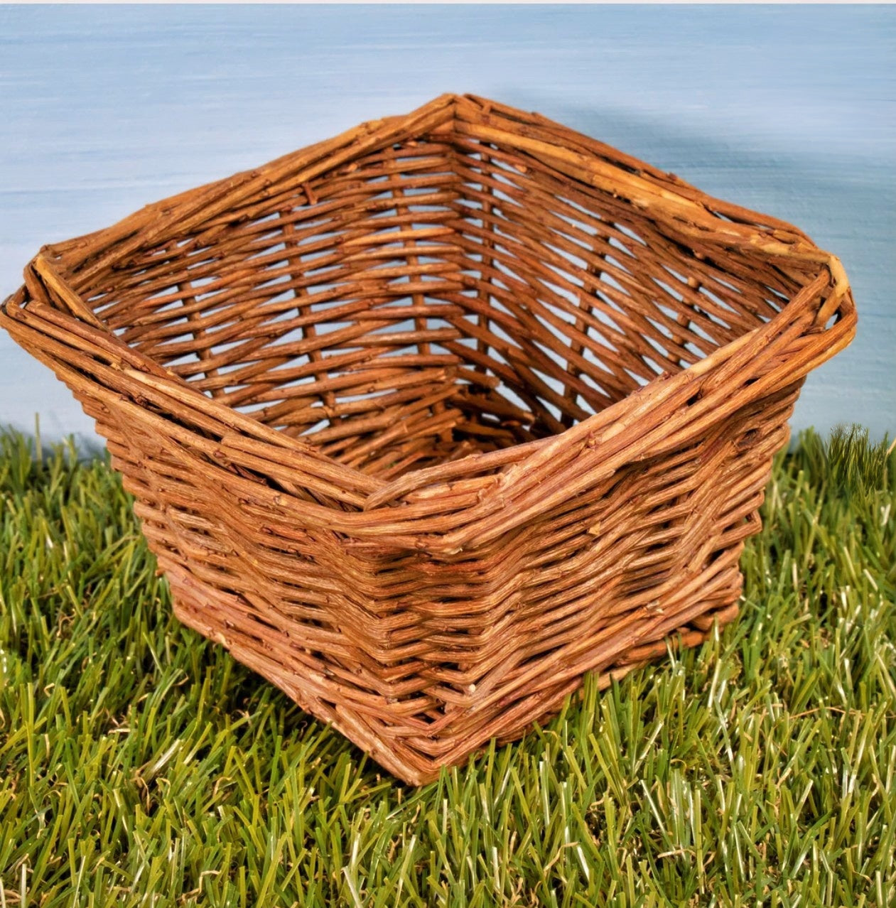 Square woven willow forage basket resting on green grass with outdoor background