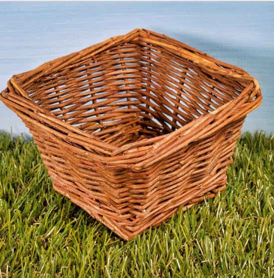 Square woven willow forage basket resting on green grass with outdoor background