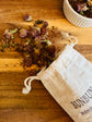 Dried red clover blossoms  spilling out onto a wooden surface with a white cotton &