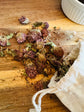 BunBun & Co dried Red Clover Blossoms spilling from a cotton drawstring bag onto a wooden surface.