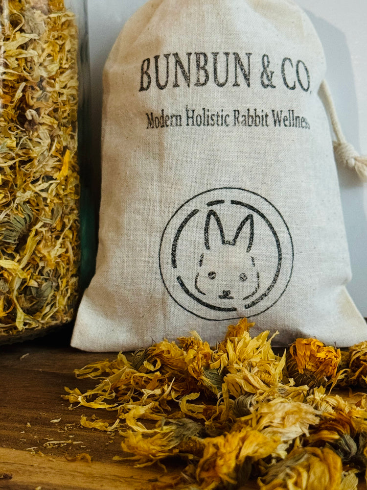 Bunbun & Co white cotton bag with rabbit emblem surrounded by dried marigold flowers on a wooden surface.