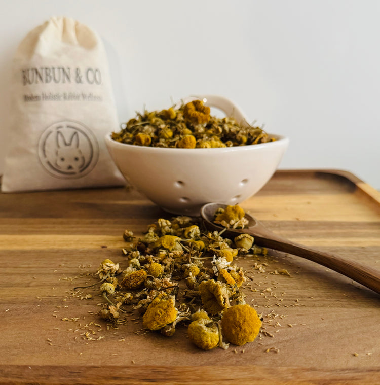 Dried  chamomile flowers in a white bowl on a wooden surface with a &