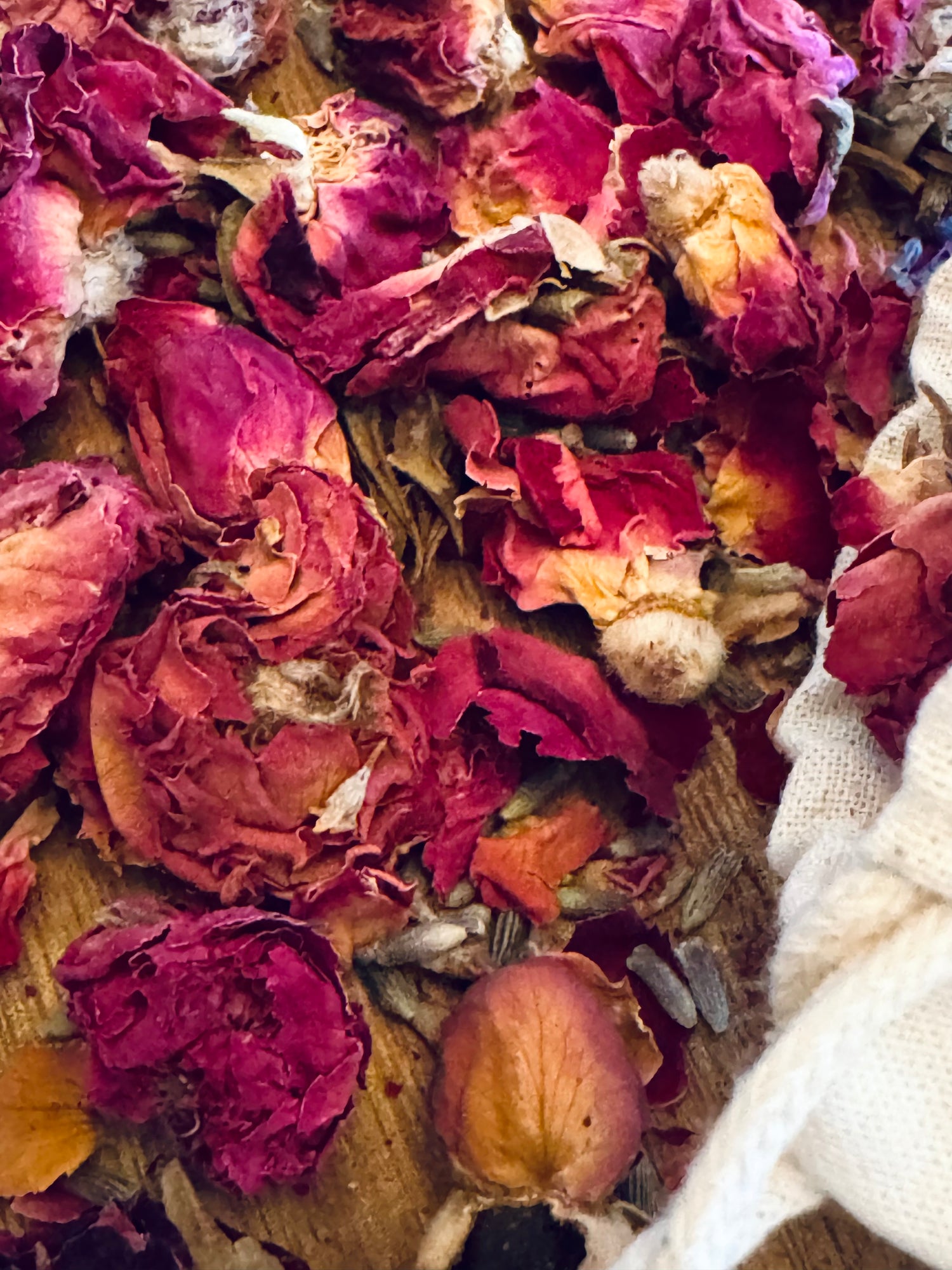 Close-up of dried red rose buds  with a white cotton bag on a wooden surface.