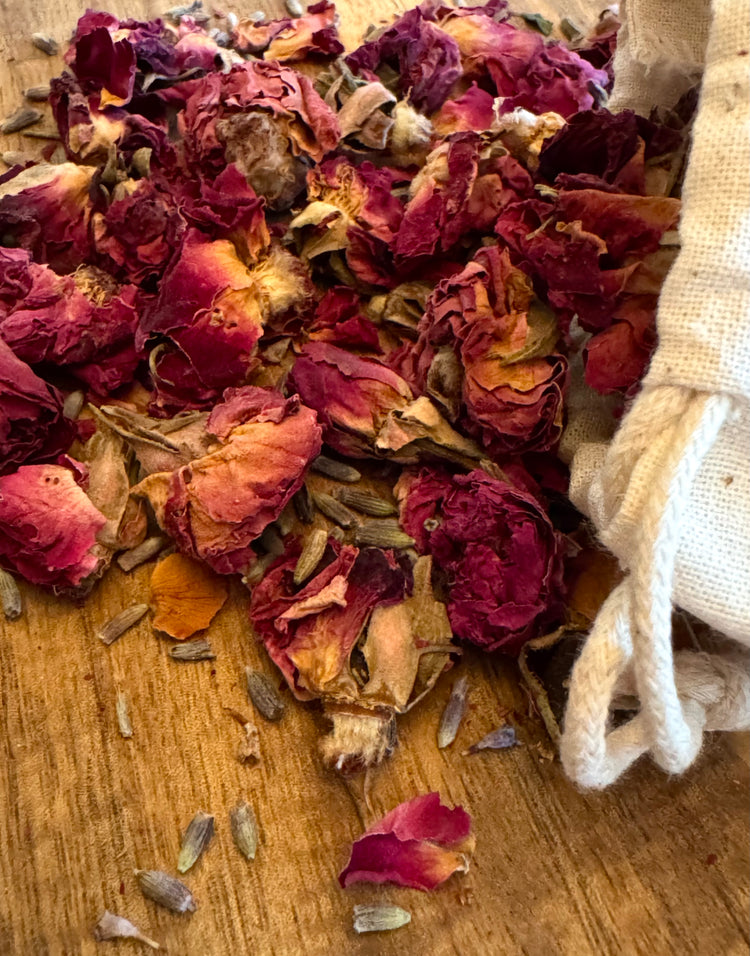 Dried red rose buds and lavender blossoms on a wooden surface with a white cotton bag.